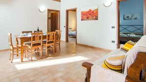 Un'ampia zona giorno con un tavolo da pranzo in legno e sedie, un divano con cuscini a righe e un letto con struttura in metallo.
