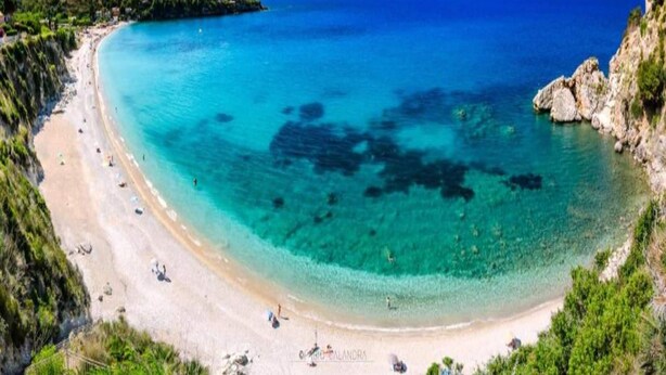 Une plage aux eaux turquoise et limpides, bordée d’un rivage sablonneux et de falaises rocheuses.