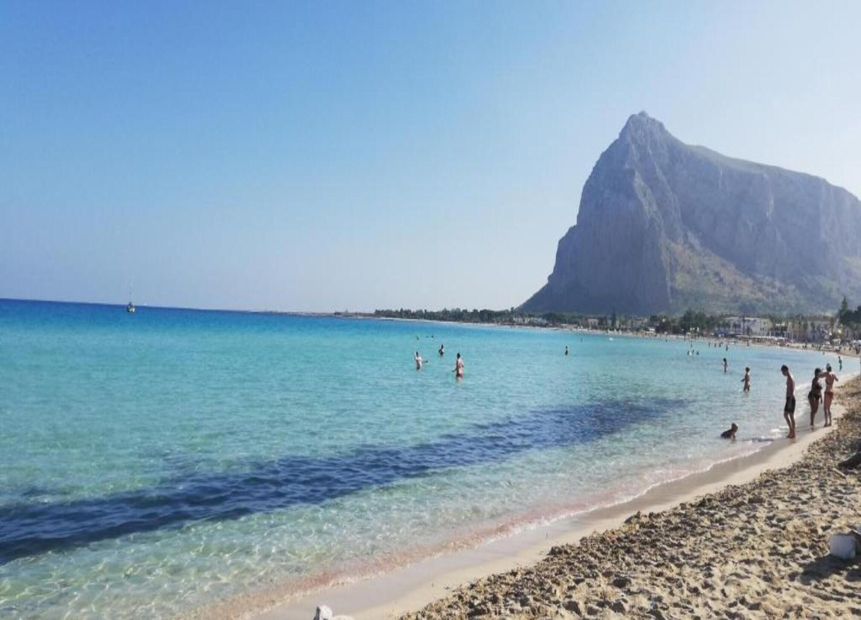 Una platja amb aigua turquesa cristal·lina, una costa rocosa i una gran muntanya al fons.