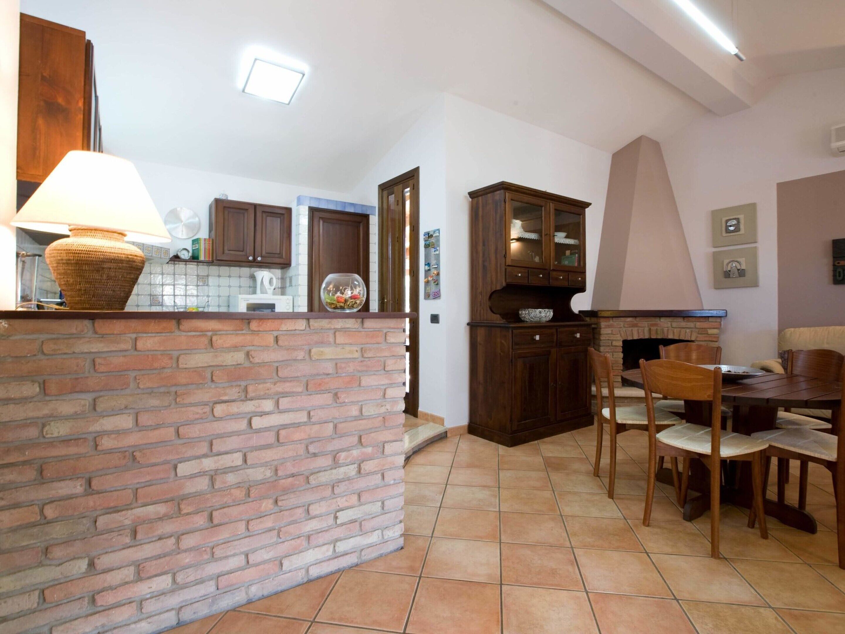 A kitchen with a brick counter, wooden cabinets, and a dining area with a table and chairs.
