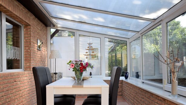 A conservatory with a brick wall, a white table, black chairs, and a vase of flowers. - Ferienhaus mit Garten in Graal-muritz (Graal Mueritz)
