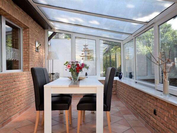 A conservatory with a brick wall, a white table, black chairs, and a vase of flowers. - Ferienhaus mit Garten in Graal-muritz (Graal Mueritz)