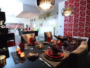 A dining area with a table set for two, featuring a modern chandelier, red and black tableware, and candles.