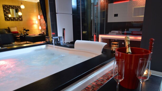 Ein modernes Badezimmer mit einem großen Spiegel, einer Badewanne und einem roten Eimer mit Sektgläsern.