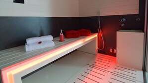 Ein moderner Wellnessraum mit warmer Fußbodenheizung, einer Massageliege und roten Handtüchern.