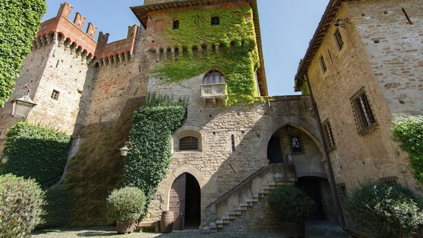 Un castillo de piedra histórico con una torre, una entrada en arco y muros cubiertos de hiedra.