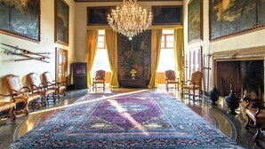 Una sala majestuosa con un gran candelabro ornamentado, una alfombra estampada y arquitectura clásica.