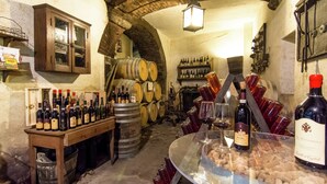 Una bodega con barriles de madera, botellas de vino y una vitrina con copas y corchos.