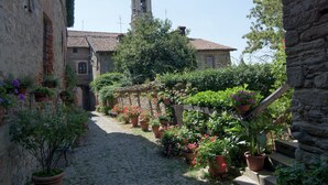 Un callejón empedrado con edificios de piedra, una torre de campanas y plantas en macetas.