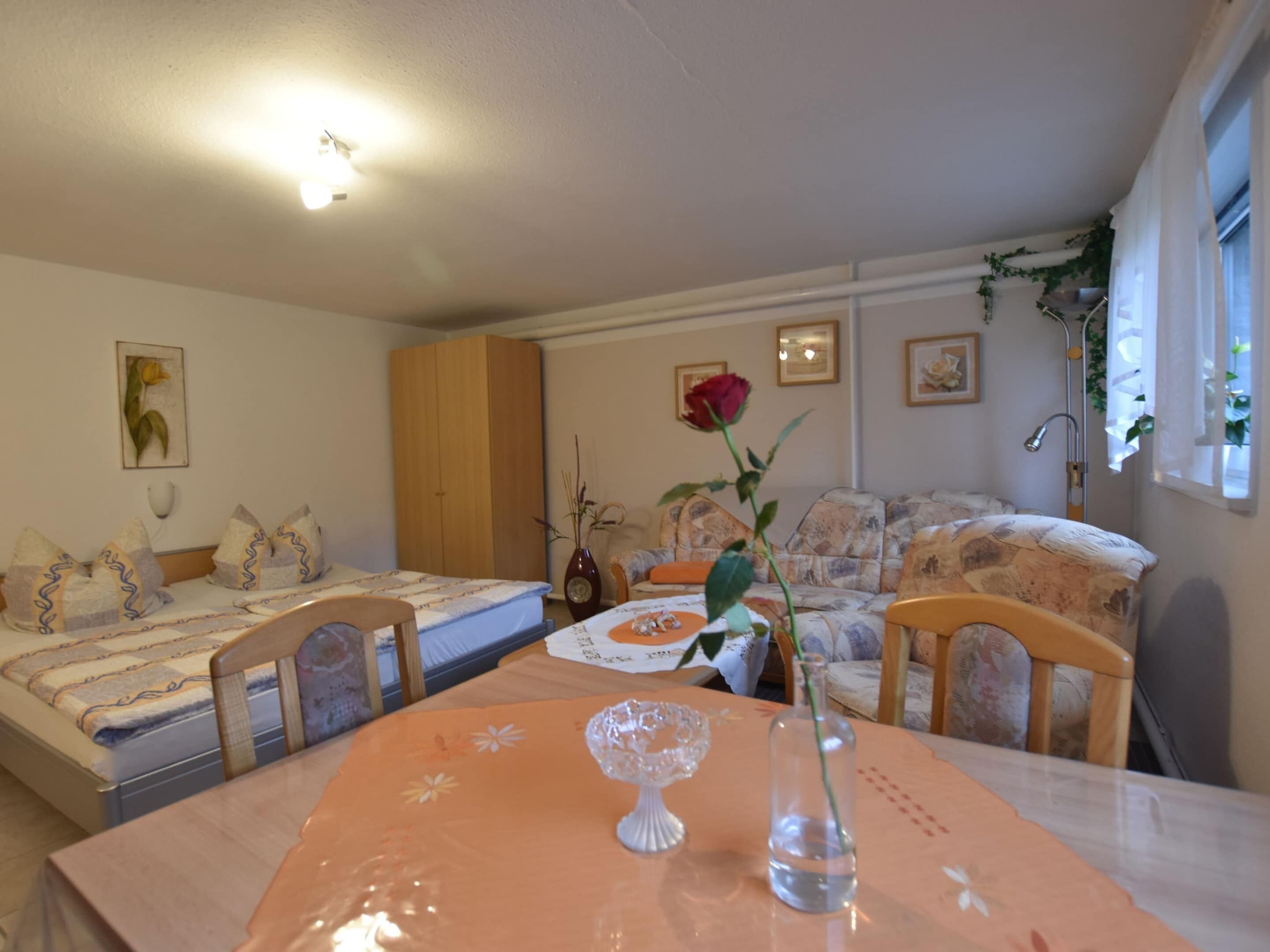 Una stanza accogliente con un letto, un divano, un tavolo da pranzo e un vaso con una rosa.