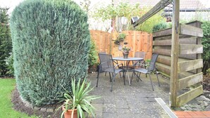 Een terras met een houten omheining, een ronde tafel met stoelen en een potplant.