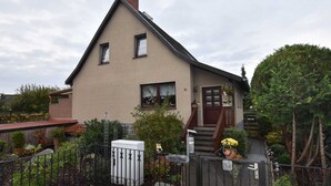 Een huis met twee verdiepingen, een schuin dak, een voortuin met trap en een brievenbus.
