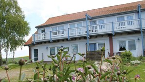 Ein zweistöckiges Haus mit rotem Ziegeldach, weißen Außenwänden und einem Balkon mit weißen Geländern.