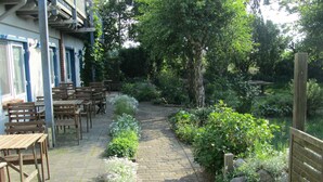Ein Garten mit einer Terrassenanlage, Holztischen und -stühlen, einem Steinweg und verschiedenen Pflanzen.