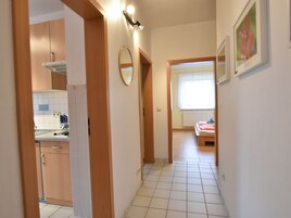 Un pasillo estrecho con una cocina a la izquierda, una cama con ventana a la derecha y un espejo en la pared.