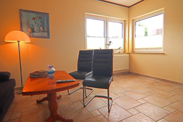 A room with two black chairs, a wooden table, a lamp, and a painting on the wall.