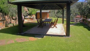 A covered patio with a table and chairs, surrounded by a stone wall and greenery. - Belvilla by OYO Leccio Lauro Quattro (Cortona)