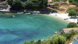 Uma área costeira com águas turquesa cristalinas, barcos e uma praia com guarda-sóis.