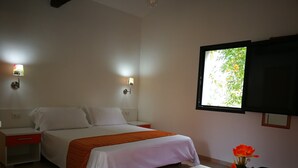 A hotel room with a bed, bedside tables, a TV, and a window with a view of greenery. - Belvilla by OYO Casa Bambu (San Pietro a Maida)