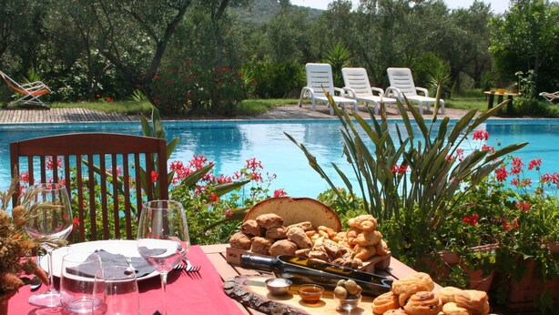 A dining table set outdoors with a view of a swimming pool and lounge chairs in the background. - Belvilla by OYO Casa Bambu (San Pietro a Maida)