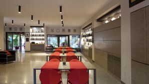 A modern restaurant interior with a long dining table, red chairs, and a bar area with shelves of bottles. - Belvilla by OYO Casa Bambu (San Pietro a Maida)