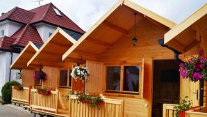 A row of wooden cabins with balconies, each featuring a window and a hanging flower basket. - Cozy Holiday Home in Mielno near Lake (Mielno)
