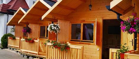A row of wooden cabins with balconies, each featuring a window and a hanging flower basket.
