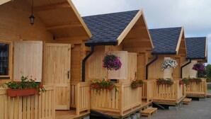 A row of wooden cabins with sloped roofs, each with a wooden door and windows, and flower planters on the front. - Cozy Holiday Home in Mielno near Lake (Mielno)