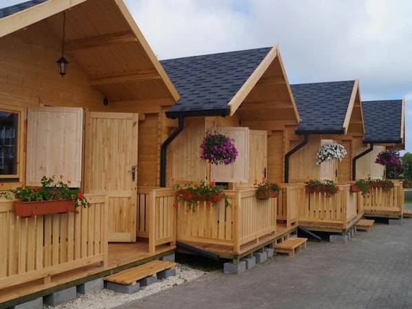 Een rij houten chalets met schuine daken, elk met een houten deur en ramen, en bloembakken aan de voorzijde.