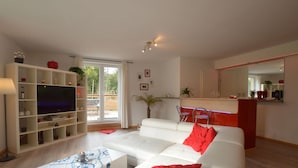 A modern living room with a white sofa, a flat-screen TV, and a dining area with red chairs. - Countryside Holiday Home in Stoumont With Terrace, Garden (Stoumont)