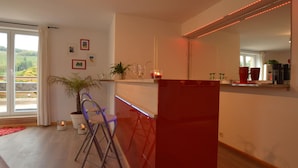 A modern kitchen with a red accent wall, a bar area, and a large window offering a view of greenery outside. - Countryside Holiday Home in Stoumont With Terrace, Garden (Stoumont)