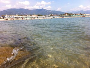 Una playa con agua cristalina, una orilla de arena y montañas al fondo.