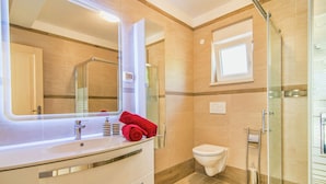 Een moderne badkamer met een grote spiegel, een witte wastafel, een toilet en een douchecabine van glas.