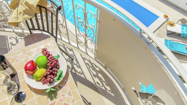 Een balkon met een zwembad, een tafel met een fruitschaal en een stoel met een handdoek.