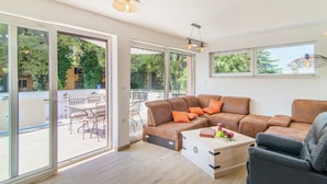 Een moderne woonkamer met een modulaire bank, een houten salontafel en een eetgedeelte zichtbaar door grote schuifdeuren.