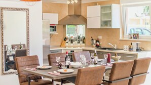 Een moderne keuken met een eethoek. Er is een grote tafel met stoelen, een keukenwerkblad en diverse keukenapparaten.