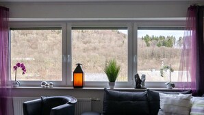 A modern living room with a sofa, two armchairs, and a window with a view of a hilly landscape. - Cozy Apartment in Willingen near Willingen Train Station (Willingen)