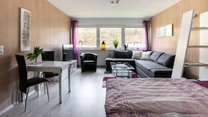 A modern, well-lit room with a dining area, a sofa, a bed, and a window with a view of trees. - Cozy Apartment in Willingen near Willingen Train Station (Willingen)