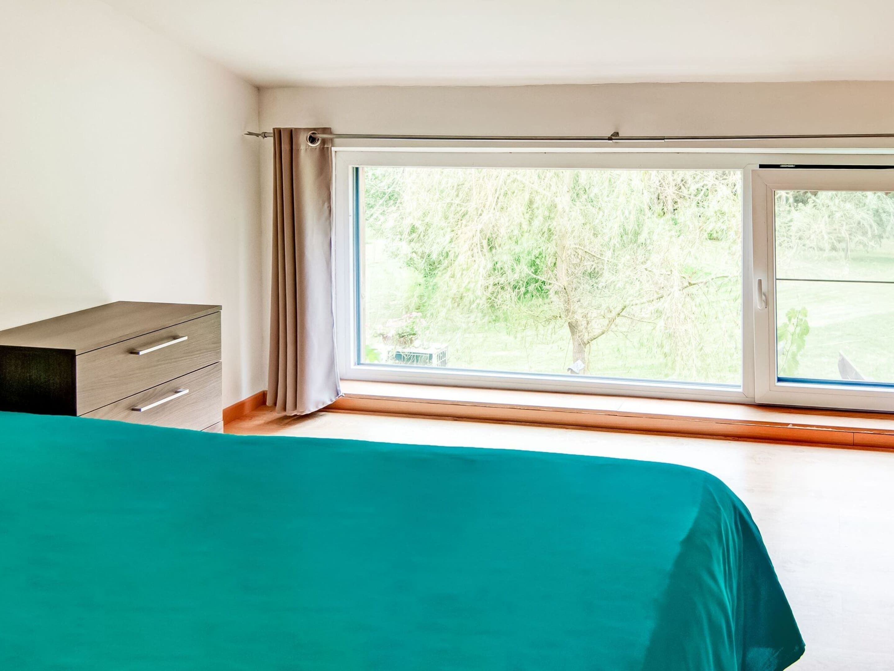 A bedroom with a large window, a bed, and a dresser.