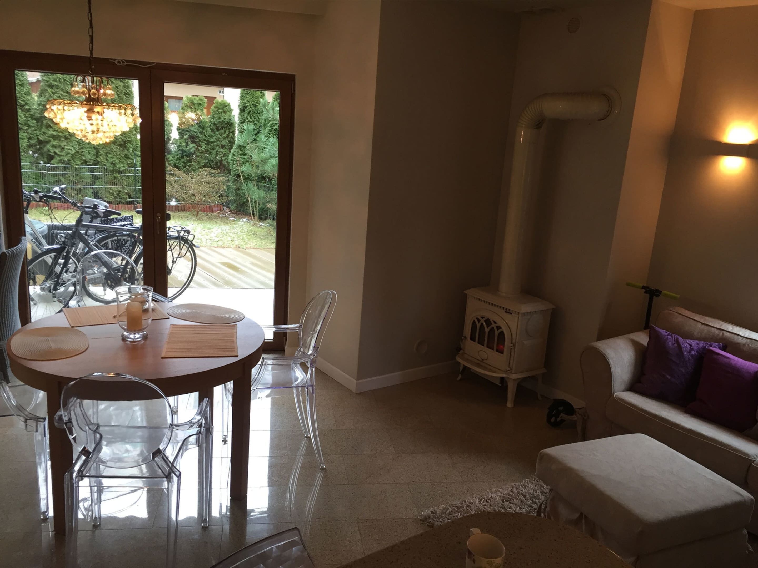 Una sala de estar acogedora con una mesa redonda, sillas transparentes, un sofá blanco y una estufa de leña.