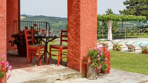 Un espace extérieur aménagé avec une table et des chaises, une vue sur la campagne et un coin piscine avec des chaises longues.