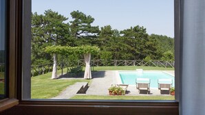Une vue depuis une fenêtre donnant sur une cour arrière avec une piscine, une pergola couverte de plantes grimpantes et une clôture en bois.