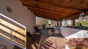 A covered patio area with wooden flooring, a white wall, a wooden bench, and outdoor furniture. - Holiday Home in Prilipje With Terrace (Jastrebarsko)