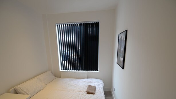 A small, neatly arranged bedroom with a single bed, a bedside table, and a window with blinds. - Spacious Apartment in Coventry near Belgrade Theatre (Coventry)
