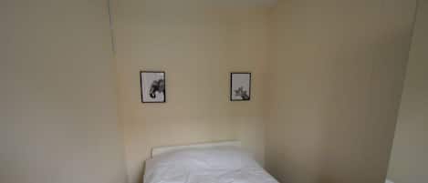 Una cama individual con ropa de cama blanca, una pared color beige y dos cuadros enmarcados.
