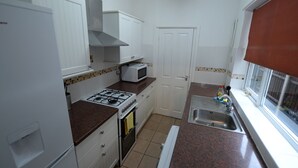 A compact kitchen with white cabinets, a gas stove, a microwave, and a sink. - Spacious Apartment in Coventry near Belgrade Theatre (Coventry)