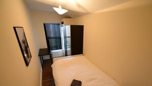 A small, neatly arranged bedroom with a single bed, a bedside table, a framed picture on the wall, and a window with blinds. - Spacious Apartment in Coventry near Belgrade Theatre (Coventry)