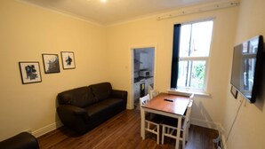 A living room with a dark brown leather sofa, a wooden dining table with two chairs, a TV mounted on the wall, and a window with curtains. - Spacious Apartment in Coventry near Belgrade Theatre (Coventry)