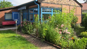 A brick house with blue-framed windows and a garden with various flowers. - Holiday Home With Terrace in Graal-muritz (Graal Mueritz)