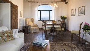 A cozy living room with a dining area, wooden ceiling beams, a large window, and a view of the sea. - Villa in Tuscany With Pool and Wine Tasting (Pergine Valdarno)